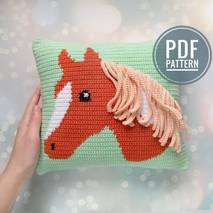 May include: Crochet pattern for a pillow featuring a horse head with a green background and peach colored mane. The pattern is available as a PDF download.