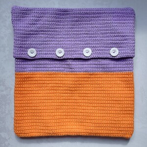 May include: A crocheted pillow with a purple top and orange bottom. The pillow has four white buttons.