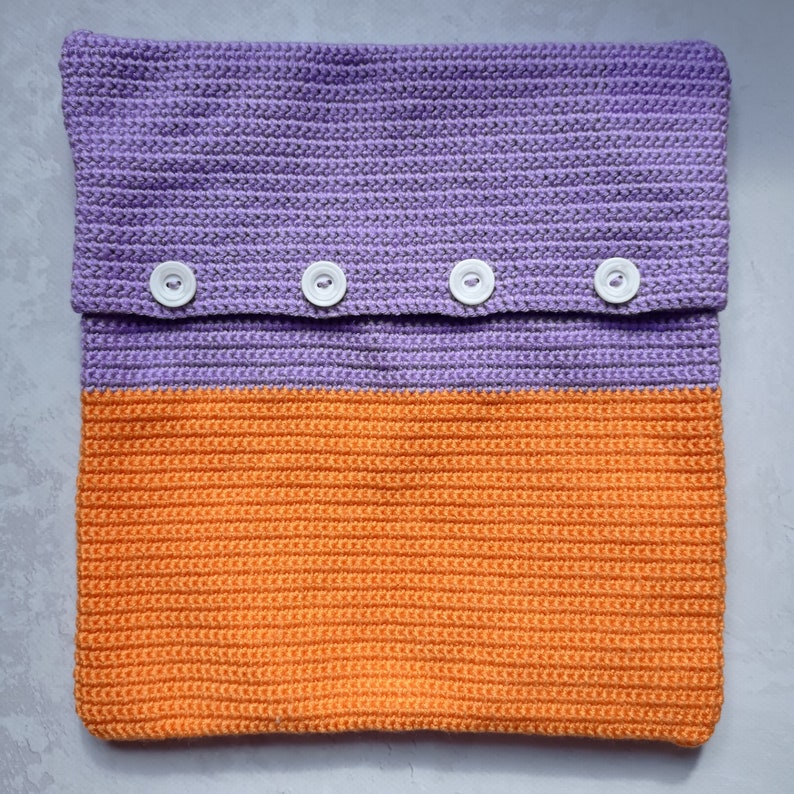 May include: A crocheted pillow with a purple top and orange bottom. The pillow has four white buttons.