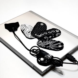 May include: A silver laptop computer with a black USB cable and five black and white fabric mouse pads with different patterns.