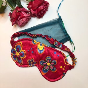 Pode incluir: Uma máscara de dormir de cetim vermelho com um padrão floral colorido. A máscara tem uma faixa elástica para um ajuste confortável.