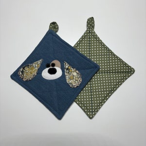 May include: Two quilted pot holders, one blue with a dog face applique and the other green with white polka dots.