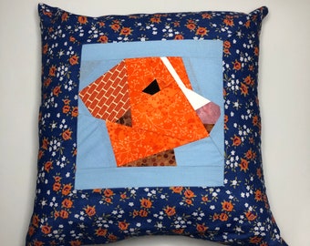 May include: A blue pillow with a floral pattern and a patchwork orange and brown dog face in the center.