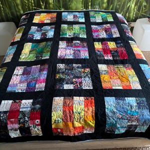 Peut inclure: Une courtepointe en patchwork composée d'une grille de carrés faits de divers morceaux de tissu multicolores, séparés par des bandes noires unies. La courtepointe présente une large gamme de motifs et de couleurs, incluant des imprimés floraux.