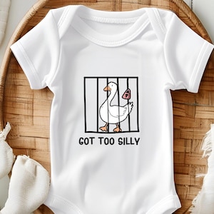 Puede incluir: Body de bebé blanco con un dibujo de un ganso de dibujos animados dentro de una jaula negra y un candado rosa. El texto "GOT TOO SILLY" está impreso en negro debajo.