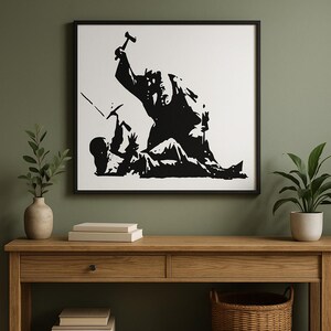 May include: Black and white framed artwork. The image shows a silhouetted scene of two figures, one with a hammer. The artwork is displayed on a wooden table, with a green wall in the background.