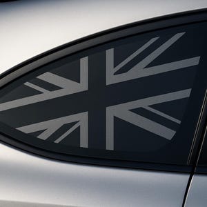 Könnte beinhalten: Ein Autofenster mit einem Union Jack-Flaggen-Design. Die Flagge ist hellgrau vor einem dunklen Hintergrund. Die Karosserie des Autos ist silberfarben.