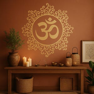 May include: A gold Om symbol, with intricate patterns, adorns a terracotta wall. A wooden table holds candles, lanterns, and bowls. A woven basket and a framed botanical print are also present.