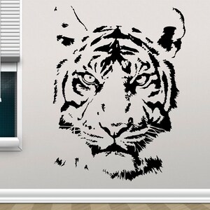 May include: Black and white silhouette of a tiger's face. The tiger's stripes are visible, and its eyes are open and intense. The image is a close-up of the tiger's face, and the background is white.