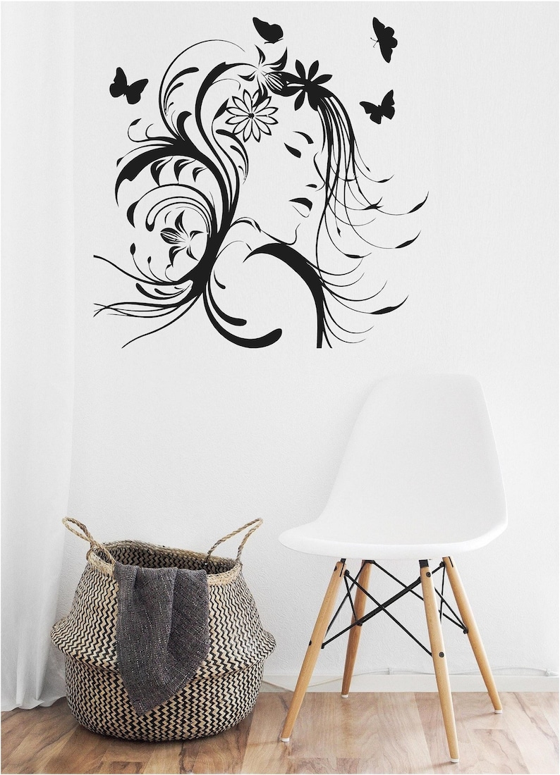 Pu&ograve; includere: Decorazione murale in bianco e nero raffigurante un volto femminile con dettagli floreali e farfalle. Una sedia bianca con gambe in legno e un cesto intrecciato con una coperta grigia sono in primo piano.