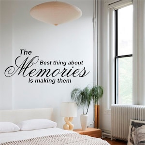 Puede incluir: Pegatina de pared en blanco y negro con el texto "The Best thing about Memories is making them". La pegatina está en una pared blanca en un dormitorio con una cama, una lámpara y una planta.