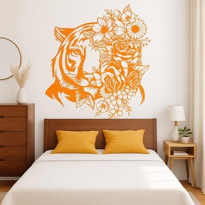 Op de afbeelding: Oranje muursticker met een tijgergezicht verweven met bloemmotieven, waaronder rozen en madeliefjes. Het ontwerp vormt een opvallend contrast met de witte muur en voegt een vleugje door de natuur geïnspireerde kunst toe aan de slaapkamerinrichting.