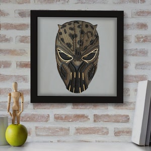 May include: Black and gold geometric design of a superhero mask in a black frame.