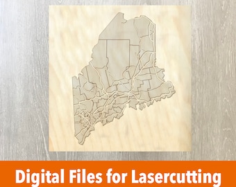 May include: A laser-cut wooden map of the state of Maine, showing the outline of the state and its counties. The map is on a light brown wooden background.