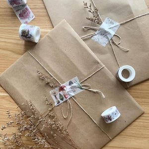 Op de afbeelding: Twee bruine papieren pakketten verpakt met touw en versierd met gedroogde bloemen en bloemenpatroon washi tape.