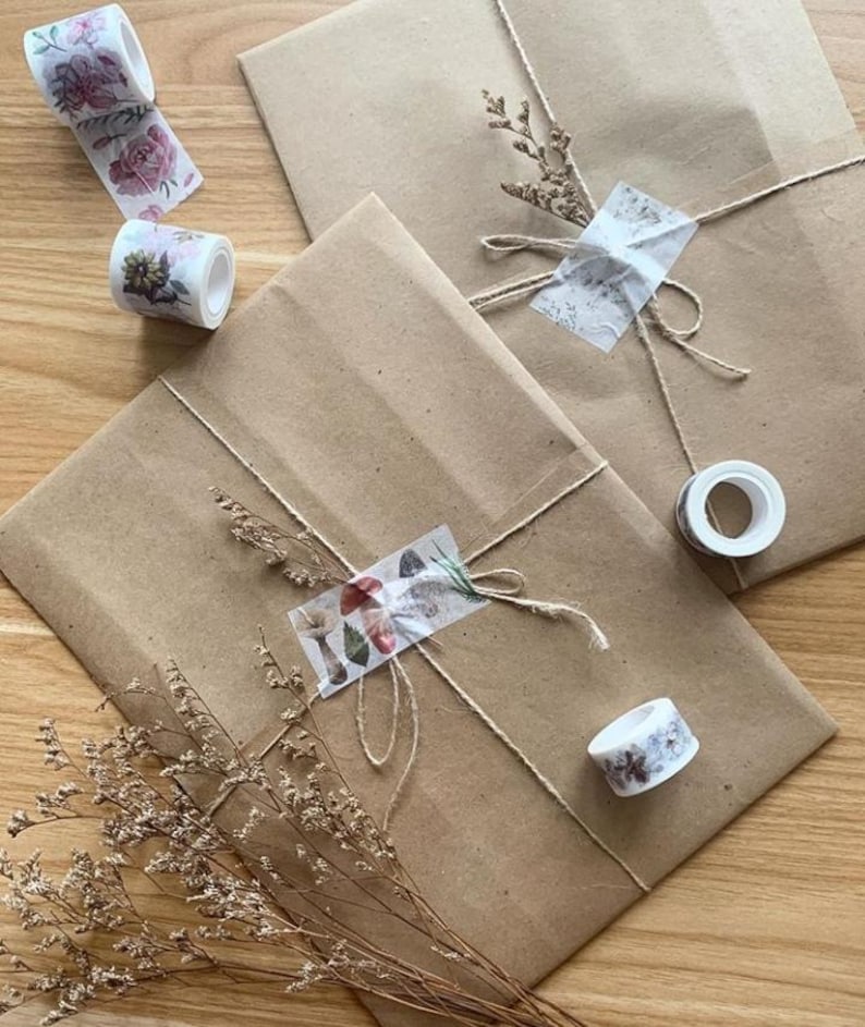 Op de afbeelding: Twee bruine papieren pakketten verpakt met touw en versierd met gedroogde bloemen en bloemenpatroon washi tape.