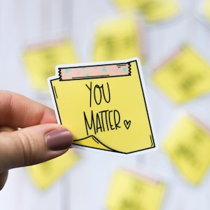 May include: A yellow sticky note with the text "You Matter" and a small heart symbol. The note is held in a hand.