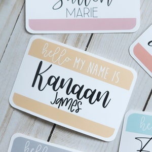 May include: A white name tag with a peach colored stripe. The text on the tag reads "hello my name is Kanaan James".
