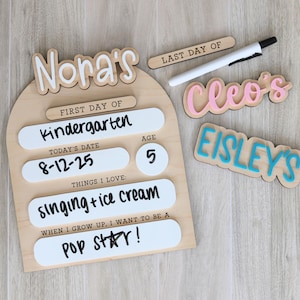 Pu&ograve; includere: Un cartello di legno con il nome "Nora's" e dettagli per il primo giorno di scuola materna, tra cui la data, l'et&agrave; e le cose che ama. Sono presenti anche cartelli in legno aggiuntivi con i nomi "Cleo's" e "Eisley's".