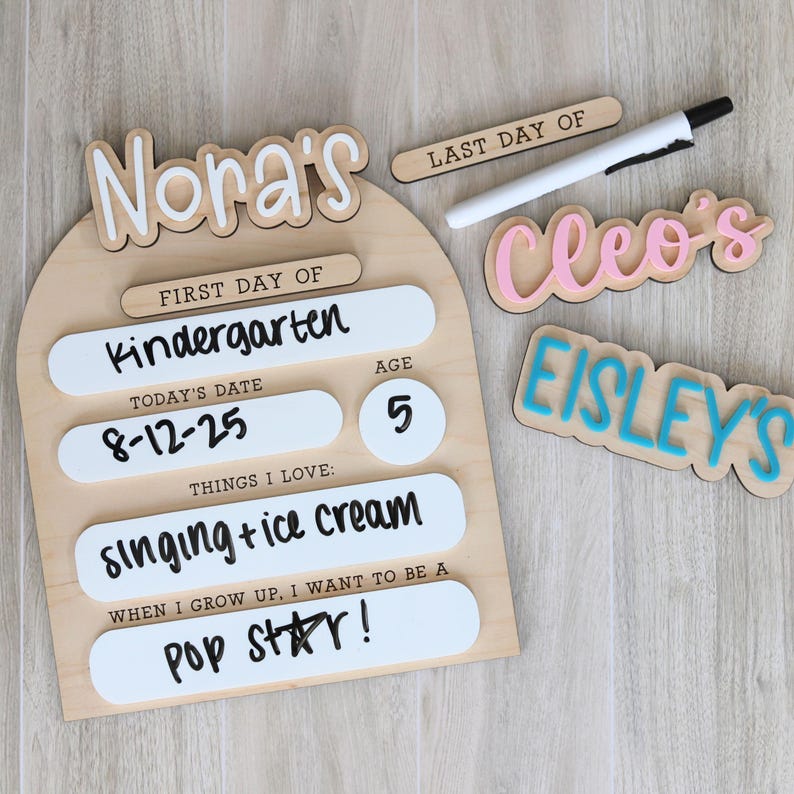 Pu&ograve; includere: Un cartello di legno con il nome "Nora's" e dettagli per il primo giorno di scuola materna, tra cui la data, l'et&agrave; e le cose che ama. Sono presenti anche cartelli in legno aggiuntivi con i nomi "Cleo's" e "Eisley's".