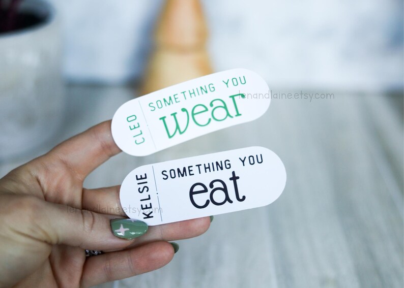 May include: Two white oval stickers with black and green text. The top sticker says "Cleo Something You Wear". The bottom sticker says "Kelsie Something You Eat".