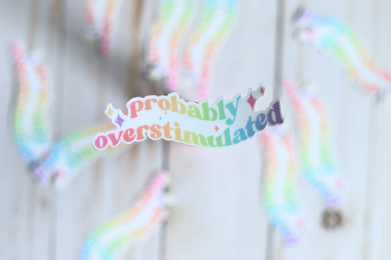 May include: A rainbow sticker with the text "probably overstimulated" in a retro font style.