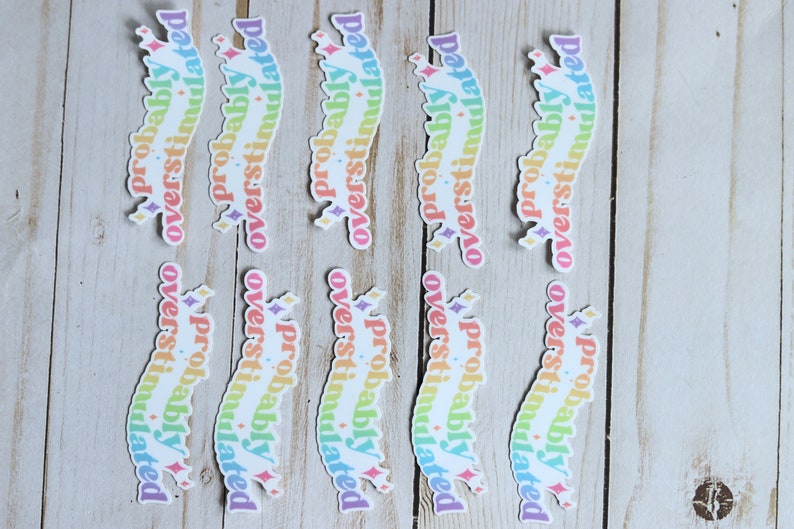 May include: Nine rainbow-colored stickers with the text "probably overstimulated" in a curved font. The stickers have a glittery finish.