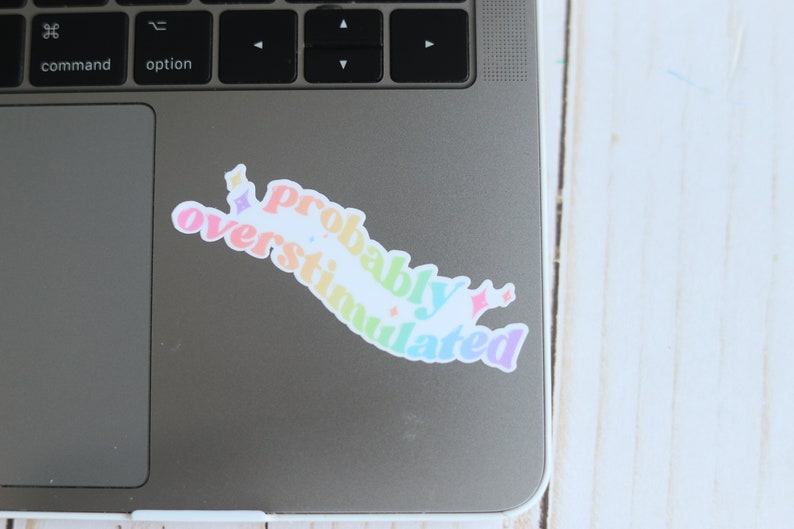 May include: A rainbow-colored sticker on a laptop that says "Probably Overstimulated" with stars around the text.