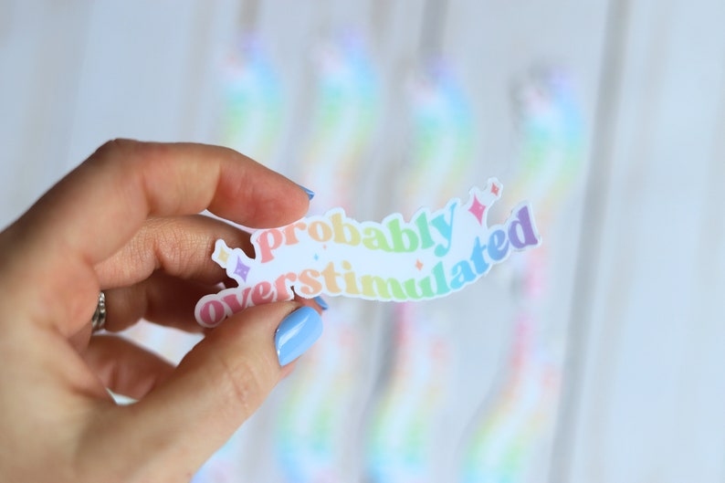 May include: A rainbow-colored sticker with the text "probably overstimulated" in a retro font style.