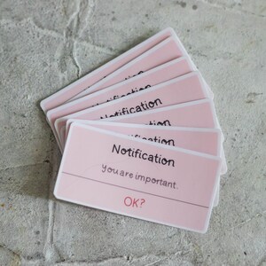 May include: A stack of pink notification stickers with white borders. The text on the sticker reads "Notification you are important. OK?"