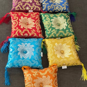 以下が含まれることがあります： 紫、青、緑、赤、黄、オレンジなど、さまざまな色で刺繍された花柄の正方形の瞑想クッションが7つあります。各クッションの中央にはボタンがあり、各コーナーにはタッセルが付いています。