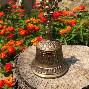Puede incluir: Una campana de metal dorada con tallas intrincadas y una parte superior decorativa. La campana está sentada sobre un tocón de árbol.