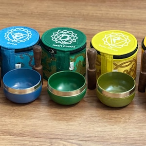May include: Set of seven singing bowls with mallets and colorful fabric carrying cases. Each bowl is decorated with a different chakra symbol and color.