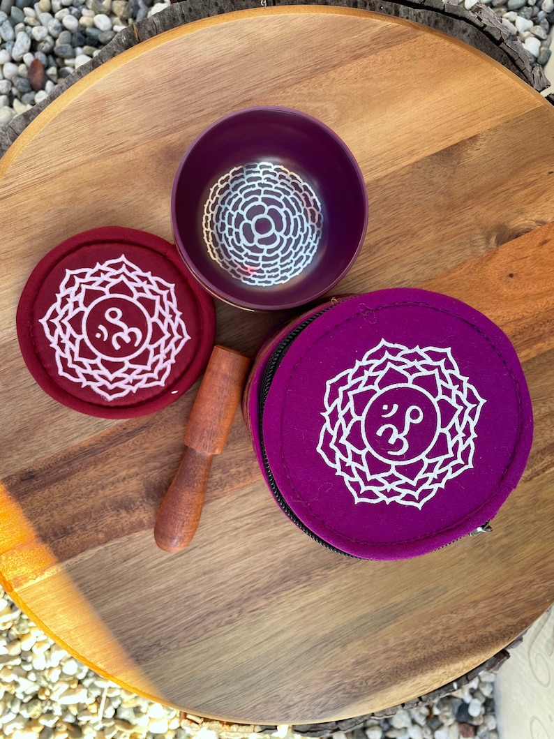 May include: Two purple singing bowls with a white mandala design and the Sanskrit symbol Om. One bowl is in a purple pouch with a white mandala design and the Sanskrit symbol Om. A wooden striker is included.