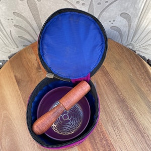 May include: A purple singing bowl set with a wooden striker, inside a purple and blue carrying case with a zipper closure.