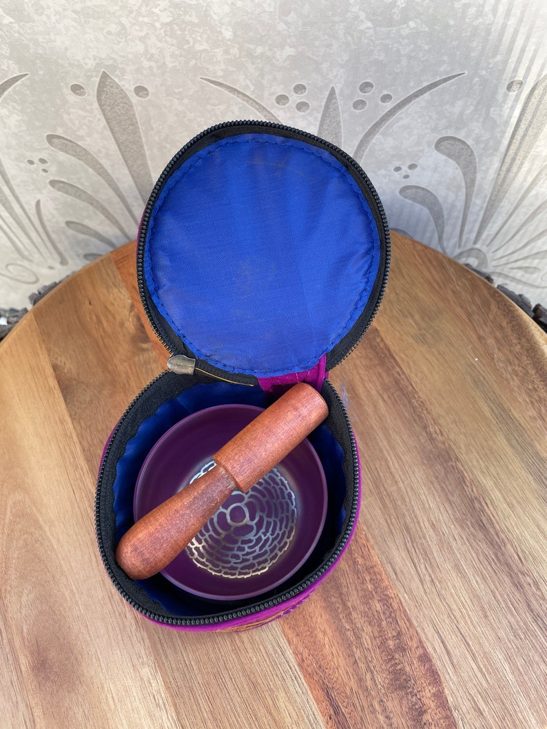May include: A purple singing bowl set with a wooden striker, inside a purple and blue carrying case with a zipper closure.