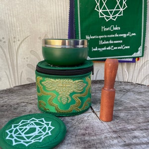 Puede incluir: Conjunto de cuenco cantor verde con un mazo de madera, una bolsa verde con bordados dorados y un coj&iacute;n verde con un s&iacute;mbolo de chakra del coraz&oacute;n blanco. El texto en la tela verde dice: "Chakra del coraz&oacute;n, Mi coraz&oacute;n est&aacute; abierto para recibir la energ&iacute;a del amor. Irradio esta esencia. Camino mi camino con facilidad y gracia."