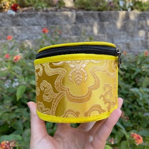 May include: A small, round, yellow zippered pouch with a black zipper and a gold floral pattern.