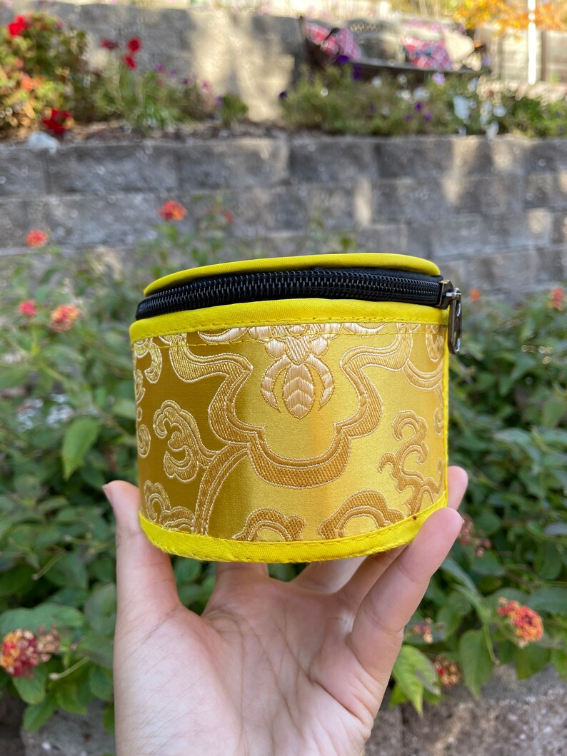 May include: A small, round, yellow zippered pouch with a black zipper and a gold floral pattern.