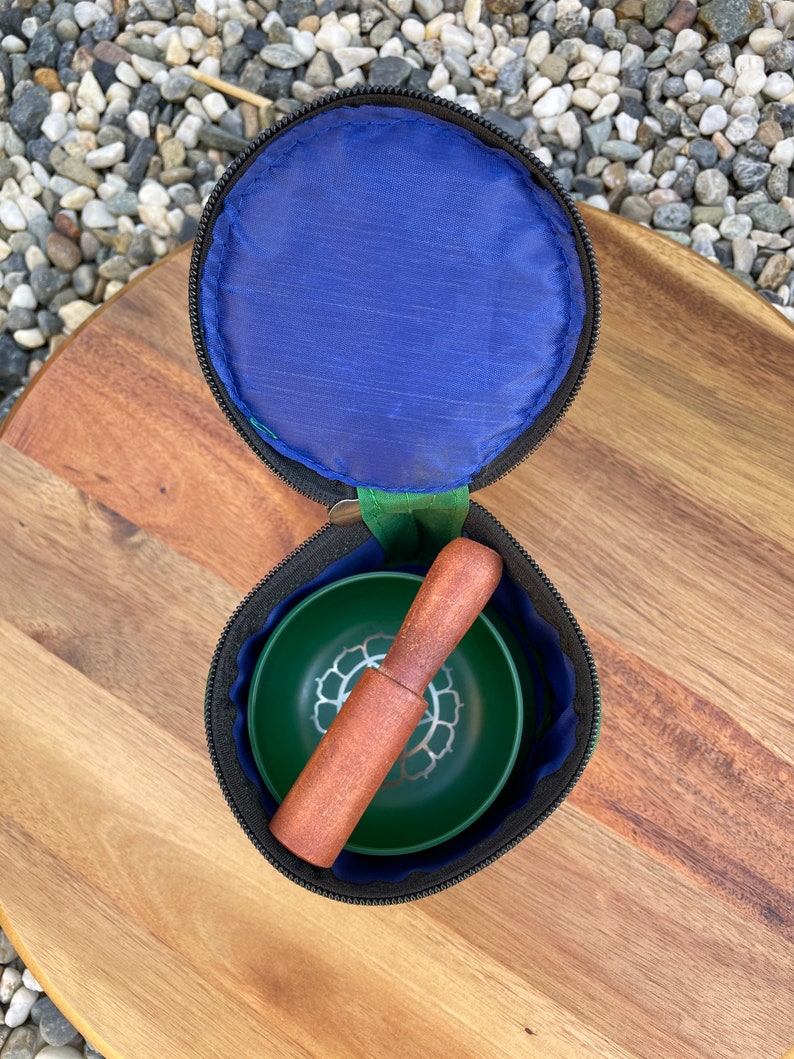 May include: A green singing bowl with a silver lotus design, a wooden striker, and a black zippered carrying case.