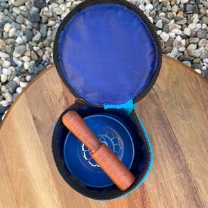 May include: A blue singing bowl with a wooden striker, both inside a blue carrying case with a zipper closure.