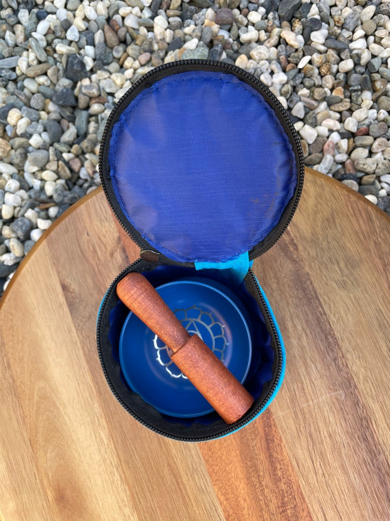 May include: A blue singing bowl with a wooden striker, both inside a blue carrying case with a zipper closure.