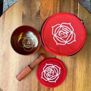 May include: A red singing bowl with a white symbol, a red mallet, and a red carrying case with a white symbol. The symbol is a white lotus flower with a triangle inside.