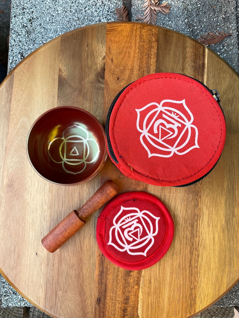 May include: A red singing bowl with a white symbol, a red mallet, and a red carrying case with a white symbol. The symbol is a white lotus flower with a triangle inside.