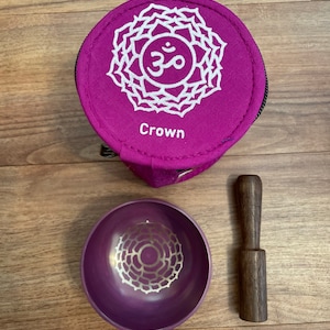 May include: Purple singing bowl with a white mandala design, a wooden striker, and a purple carrying case with a white mandala design and the word "Crown" printed on it.