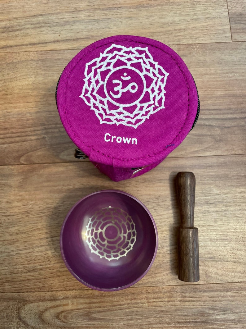 May include: Purple singing bowl with a white mandala design, a wooden striker, and a purple carrying case with a white mandala design and the word "Crown" printed on it.