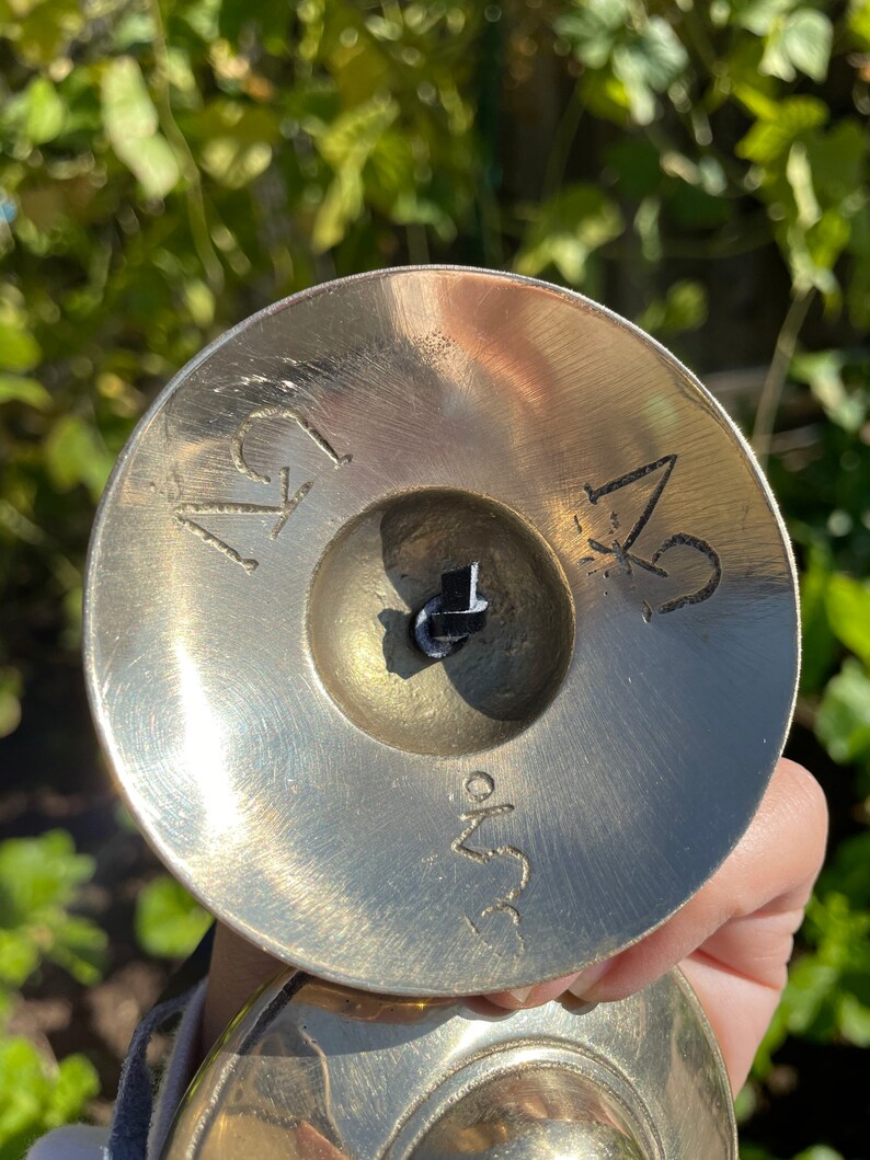 May include: A pair of small, round, brass cymbals with a black string connecting them. The cymbals have the numbers "1" and "2" engraved on them, along with the text "3.5" on the bottom.