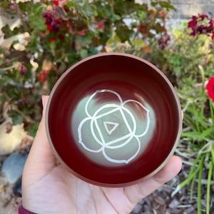 May include: A red singing bowl with a white symbol of the heart chakra, a lotus flower with a triangle inside.