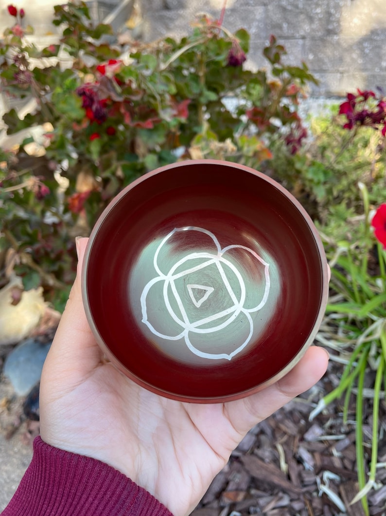 May include: A red singing bowl with a white symbol of the heart chakra, a lotus flower with a triangle inside.
