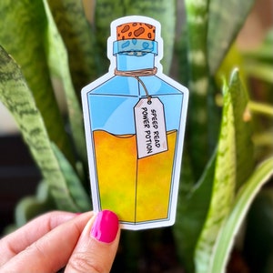 Può includere: Un adesivo di una bottiglia di vetro blu con un tappo di sughero e un liquido giallo all'interno. La bottiglia ha un'etichetta che recita "Speed Read Power Potion".